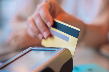 Close-up of a hand holding a credit card, performing a transaction on a contactless payment terminal. Modern technology representing convenience, cashless payments, and digital banking.