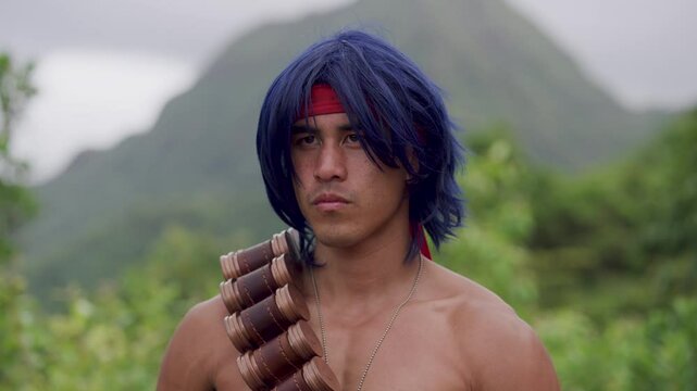 Warrior with blue hair and ammunition belt mumbling angrily in tropical area - medium shot