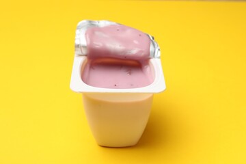 Delicious yogurt in plastic cup on yellow background, closeup