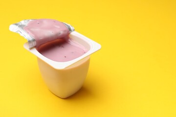 Delicious yogurt in plastic cup on yellow background, closeup. Space for text