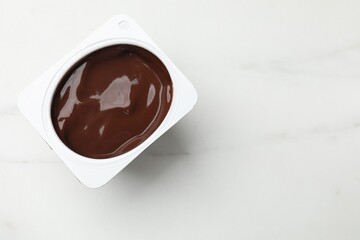 Delicious chocolate yogurt in plastic cup on light marble table, top view. Space for text