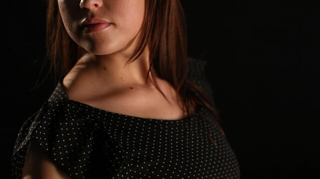 A graceful close-up portrait of a woman in a black polka dot dress, showcasing her neckline, lips, and soft hair movement against a dark background with subtle dramatic lighting