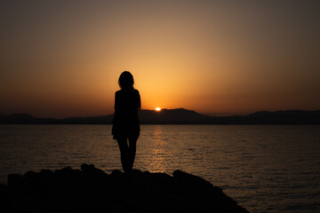 Fototapeta premium Silhouette of a Woman Watching a Peaceful Sunset Over the Sea