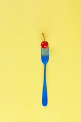 Blue Fork with a Red Cherry Against a Vibrant Yellow Background