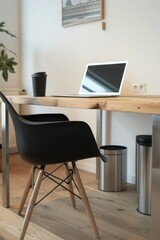 A shot of an office desk with black chair, white wall and wood floor