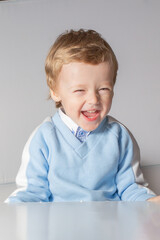 Emotional baby in shirt and blue jumper on white background