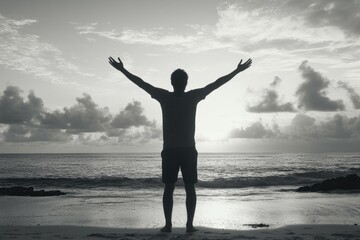 Fototapeta premium Silhouette of a person with arms raised in joy, looking towards the sunset on a beach.