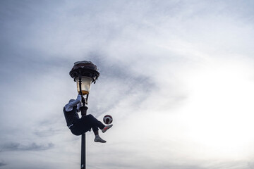 Boy entertaining tourists by hanging on a lamppost playing with a ball, Paris, France