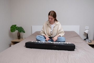 Young woman playing electronic piano at home. A red-haired girl learns to play the synthesiser.
