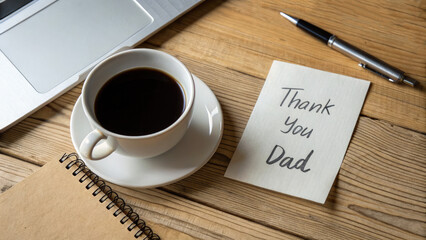 A steaming cup of coffee sits on a wooden desk beside a notebook with a heartfelt message for Dad. Office supplies and a laptop complete the scene, suggesting a productive and loving workspace