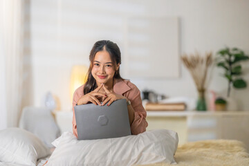 Woman working on a laptop in a cozy bedroom during evening hours while enjoying a relaxed atmosphere