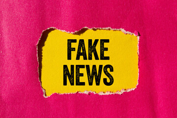 Fake news message written on ripped torn pink paper on yellow background. Conceptual fake news...