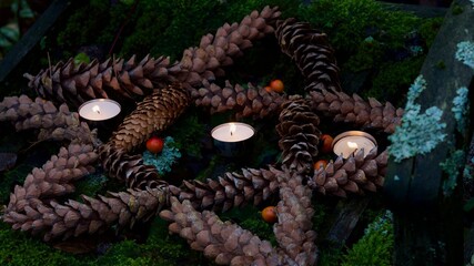 Detail eines Pentagrammes aus Tannenzapfen. Brennende Teelichter.