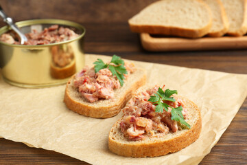 Sandwiches with canned meat and parsley on wooden table, closeup