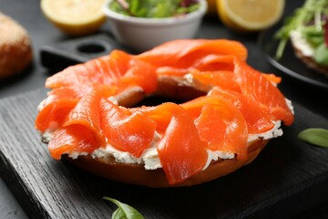 Delicious bagel with salmon and cream cheese n black table, closeup