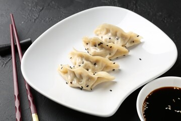Delicious gyoza dumplings with sesame seeds served on black table, closeup