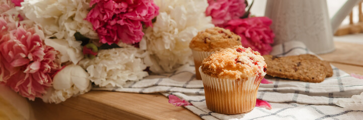 The kitchen countertop is decorated with peonies. The interior is decorated with spring flowers. Pink peonies and sweet cupcakes on a wooden countertop. Interior details.