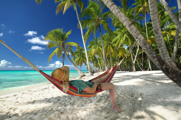happy woman relaxing on a colorful hammock on a tropical beach with palms and turquoise sea	

