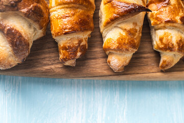 Croissants on a wooden board on a blue background. Copyspace, place for text.