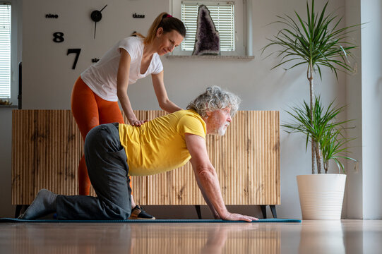 Personal trainer or physiotherapist helping an elderly man with yoga practice
