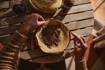 Person Preparing a Crepe with Chocolate Spread at a Wooden Table