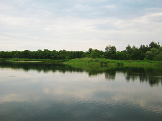 Peaceful lake reflecting cloudy sky and lush green trees. Perfect for a relaxing escape.