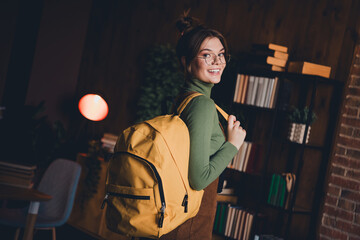 Young woman in cozy green sweater with large yellow backpack, enjoying a peaceful evening of study indoors