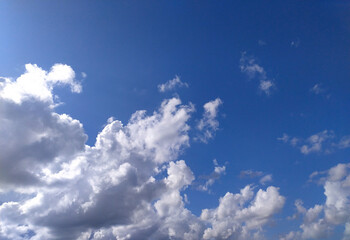 A clear blue sky with fluffy white clouds drifting lazily during a sunny afternoon in a serene outdoor setting