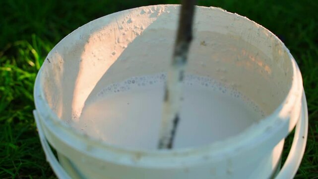 Mixing white liquid for painting tree trunks, close-up slow motion. Gardener preparing for the season in the garden