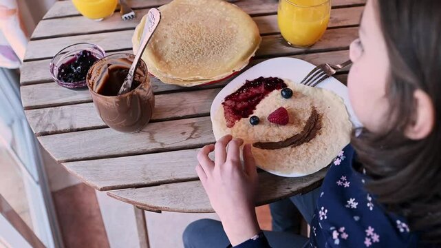 Girl Making a Smiley Face Pancake with Toppings for Shrove Tuesday