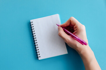 Female hands with perfect manicure holding pen and spiral notebook as a mockup for your design. Blue background, flat style