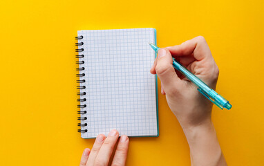 Female hands with perfect manicure holding pen and spiral notebook as a mockup for your design. Yellow background, flat style