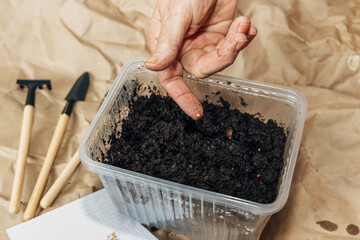 Kraft paper background, fertile soil and garden tools, top view. Hands planting seeds