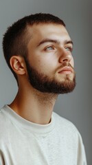 Obraz premium Confident European Man in White Soccer Jersey with Buzzcut and Beard Against Grey Background
