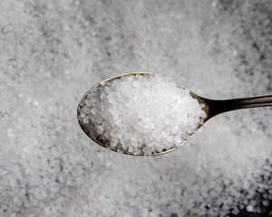 A metal spoon with salt and a pile of salt next to it. Table salt.