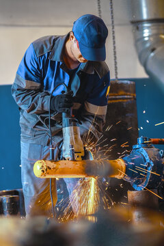 Male worker grinding metal pipe in industrial setting with safety gear.