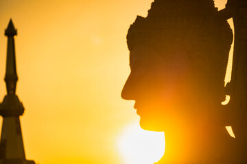 Sunset Silhouette of a Majestic Thai Temple and Statue with Golden Sky at Phetchabun, Thailand.