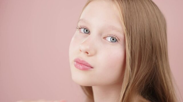 Close-up portrait of a beautiful girl of Gen Alpha with healthy facial skin on pink background. Pretty blonde girl poses looking at camera. Concept of cosmetics, advertisement for teenagers or kids