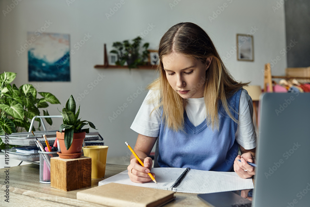 Wall mural A teenage girl focuses on her studies while surrounded by personal touches in her cozy room.