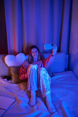 Obraz premium A teenage girl enjoys an evening in her stylish room, capturing a joyful selfie amidst soft lights.