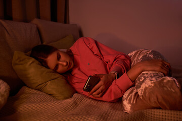 A young girl unwinds in her stylish room, engrossed in her smartphone as evening falls.