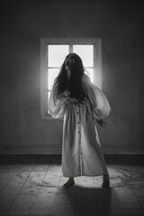 Naklejka premium Terrifying woman in white flowing gown, long claws, with open mouth screaming in a darkened room, evoking a sense of possession and dark mysticism. Concept of mystery, fantasy, supernatural creation