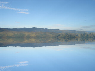Mountain range reflecting on calm water surface under blue sky