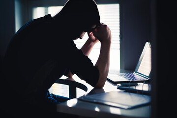 Stress at work. Tired man with anxiety. Sad office worker with laptop. Frustrated university or college student. Dark silhouette of  anxious person. Home computer. Bad problem with business.