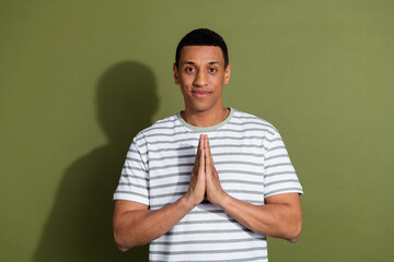 Photo of attractive funny guy wear striped t-shirt praying emtpy space isolated khaki color...