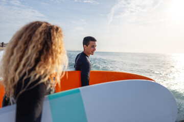 Fototapeta premium Fit couple surfing at sunset. Friends having fun inside ocean. Extreme sport and vacation concept