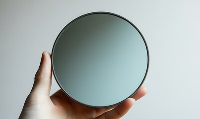 A hand holding a round mirror with a gray reflection
