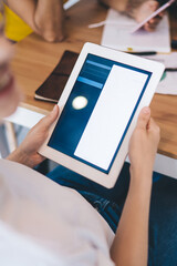 Crop positive female using tablet at table with coworkers