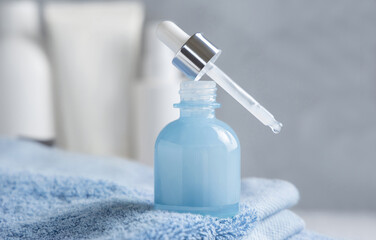 Drop falling from pipette set on opened blue dropper bottle on blue towel close up, mockup