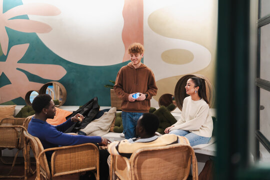 Friends sit together in a cafe with vibrant, artistic wall designs, engaging in a cheerful discussion and sharing a relaxed moment in a modern and sociable environment.